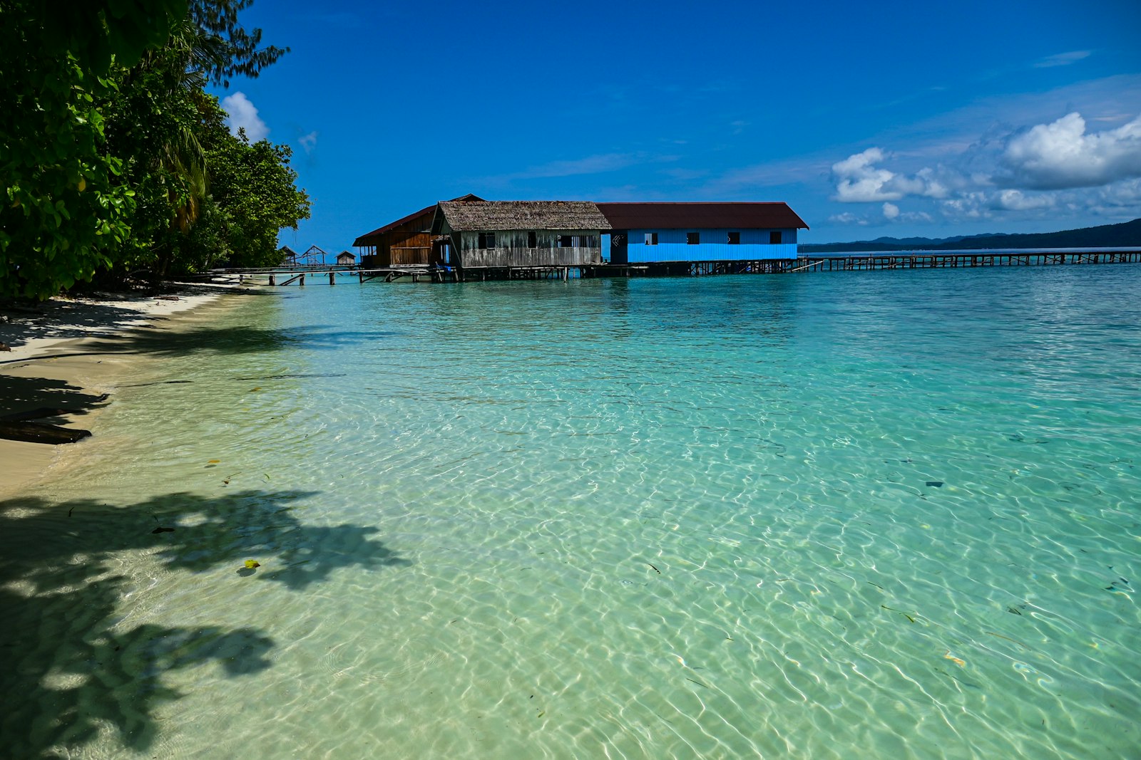 A beach with clear blue water and a hut in the distance