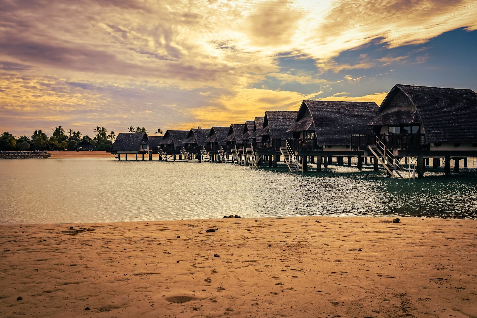 Overwater bungalows line a calm sea at sunset.